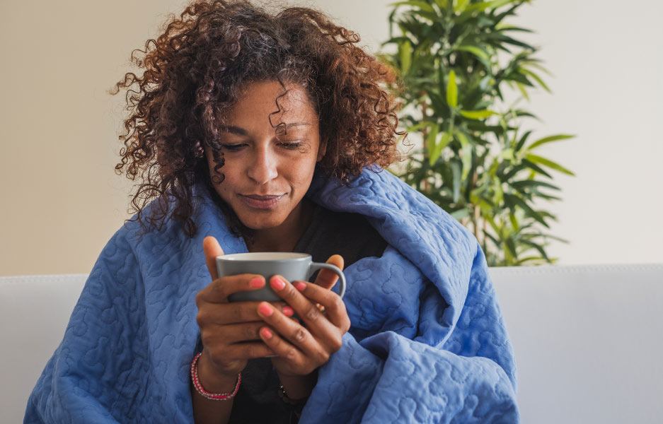 woman wrapped in a blanket clasping a cup of hot liquid